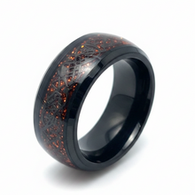 Load image into Gallery viewer, A black stainless steel band ring featuring an intricate Celtic knot pattern over a textured, red speckled inlay, shown on a clean white background.