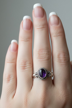 Load image into Gallery viewer, sterling silver ring with a amethyst gemstone oval cabochon stone, with a display of silver rings in the background.
