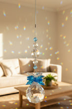 Load image into Gallery viewer, A hanging crystal suncatcher ornament with a faceted crystal ball, blue and clear crystal round beads on a thin wire , shown against an indoor wall background.
