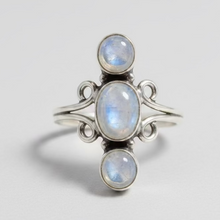 Load image into Gallery viewer, A sterling silver ring with three stacked, bezel-set round white moonstone gemstones, resting on a polished 
