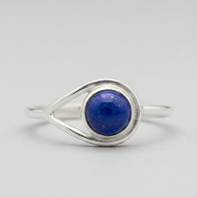 Load image into Gallery viewer, A sterling silver ring featuring a round,  lapis lazuli stone in a bezel setting, with a unique split-band design wrapping around the top, shown on a neutral light gray background.
